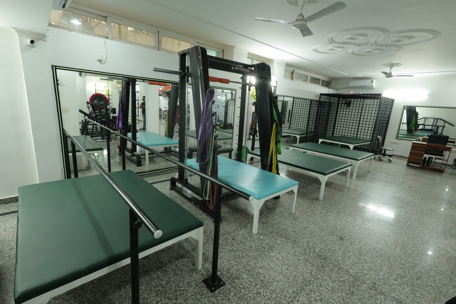 Wide view of the therapy floor at Neuranta, Sector 39 Gurugram, with parallel bars, a row of treatment plinths, wall mirrors and the suspension cage