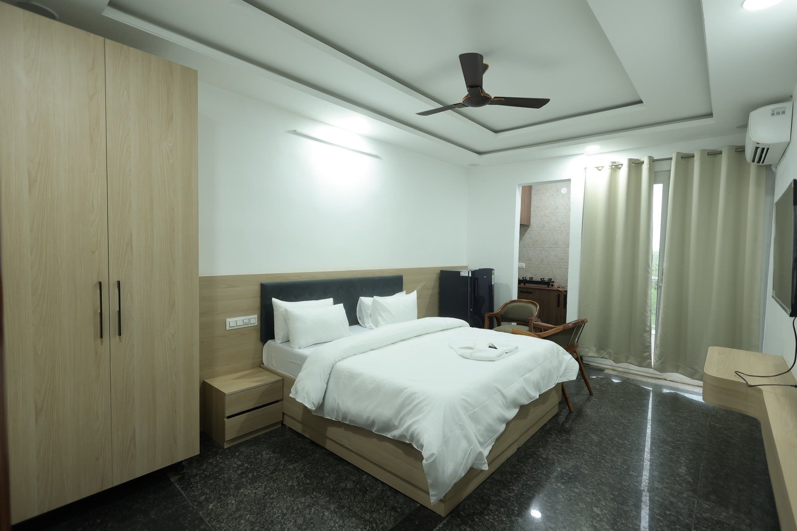 Inpatient room at Neuranta, Gurugram, with a double bed, full-height wardrobe, seating and a doorway through to a private kitchenette