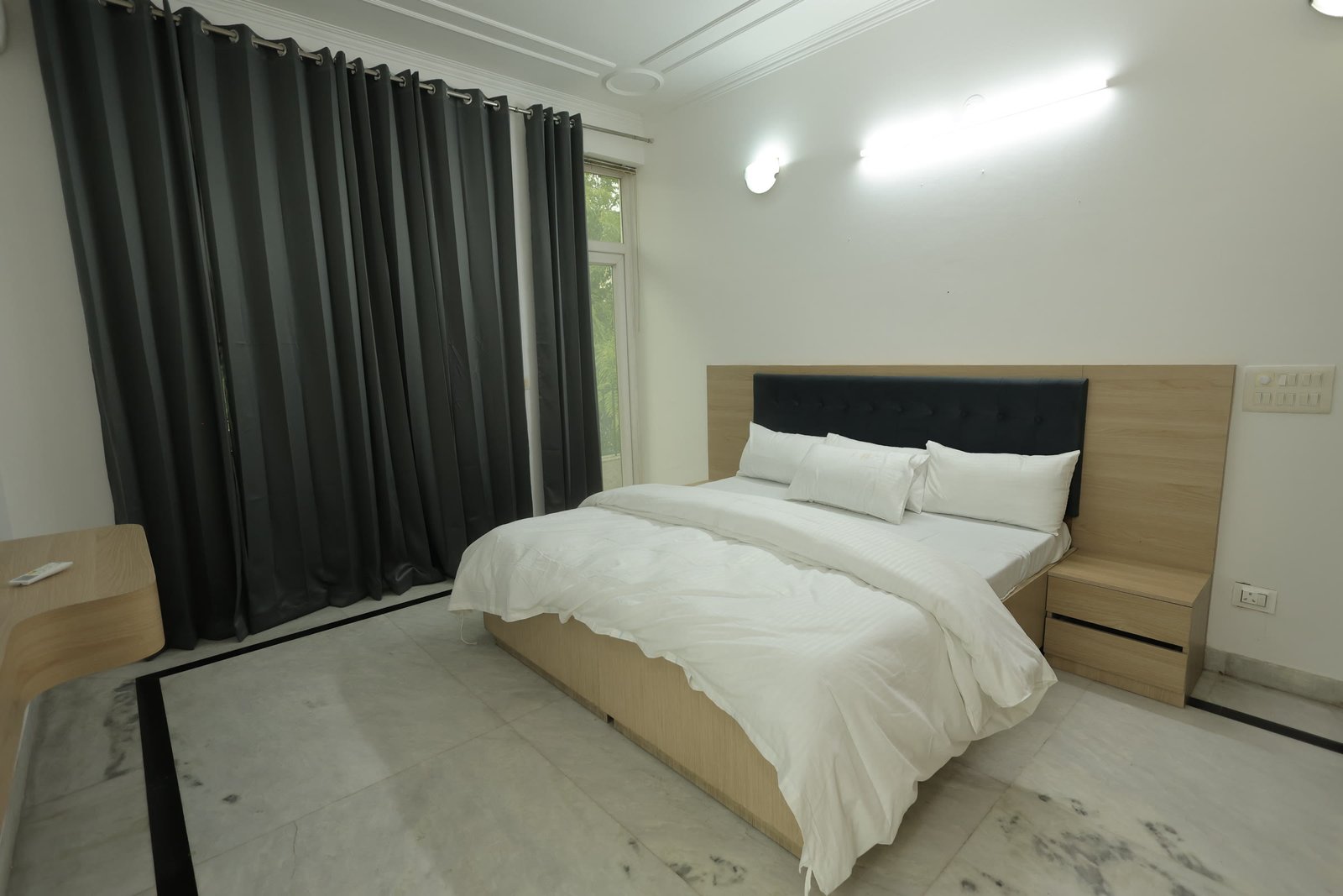 Bedroom in the inpatient suite at Neuranta rehabilitation centre, Sector 39 Gurugram, with a double bed, bedside storage and a window onto trees
