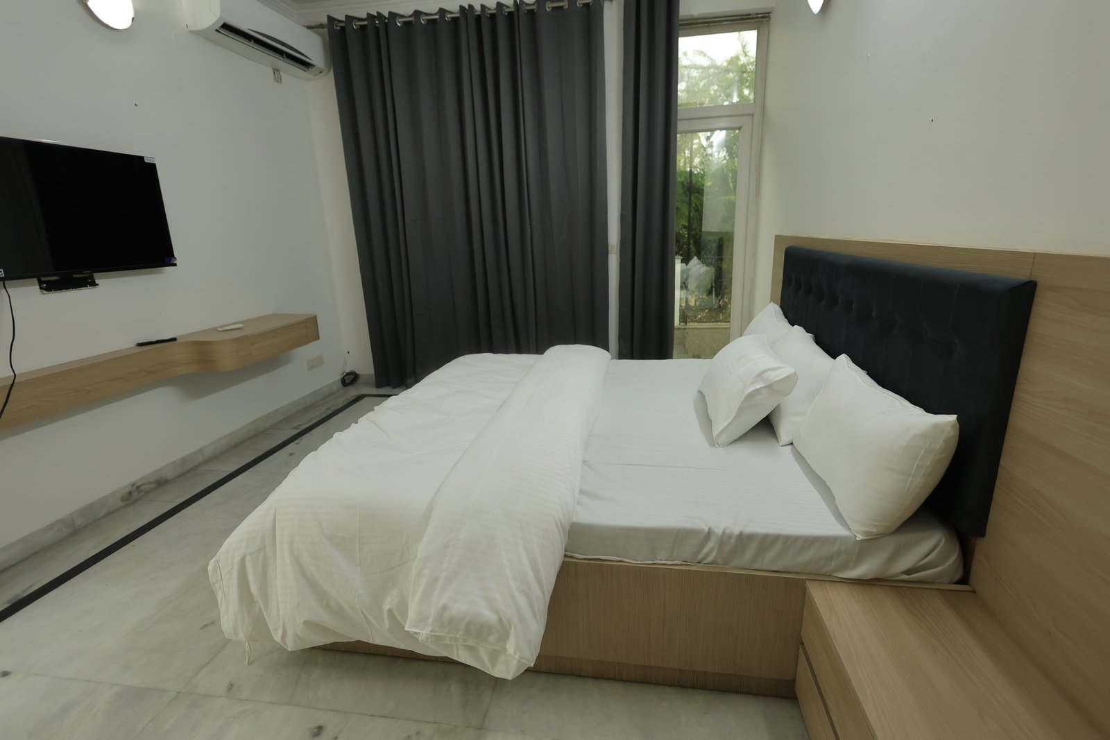 Inpatient suite bedroom at Neuranta, Gurugram, showing a wall-mounted television and a long wooden ledge opposite the bed