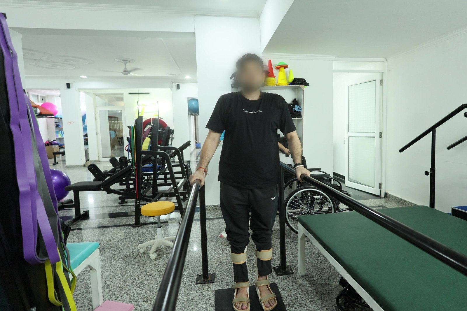 A patient practising supported standing and walking between the parallel bars, wearing knee orthoses, in the neuro rehabilitation gym at Neuranta, Sector 39 Gurugram