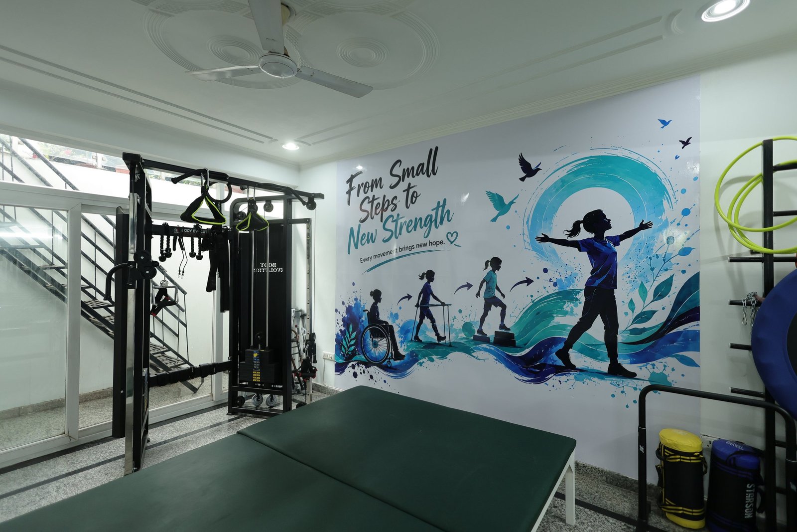 Main therapy gym at Neuranta rehabilitation centre in Sector 39, Gurugram, with treatment plinths, a multi-station gym and a painted mural reading From Small Steps to New Strength